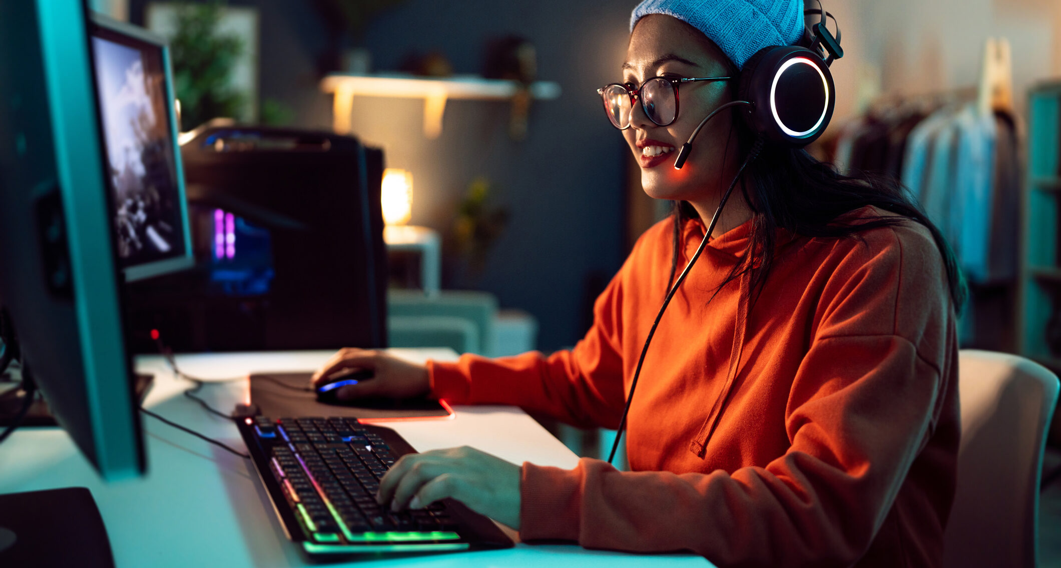 Young female gamer and streamer of Asian ethnicity, playing FPS video games on the computer in her LED-lit room