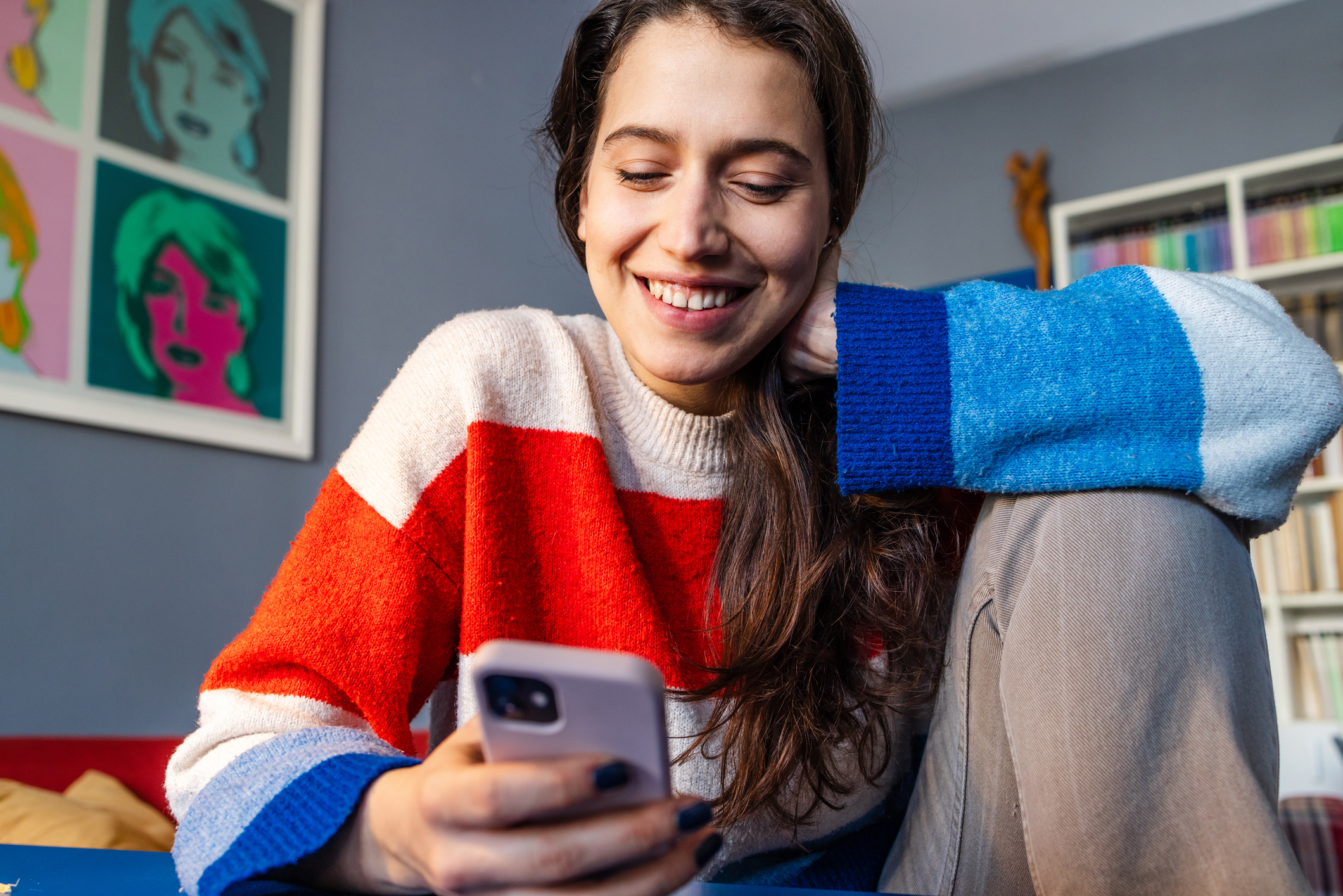A cheerful woman sitting comfortably at the desk and having online communication on her mobile phone