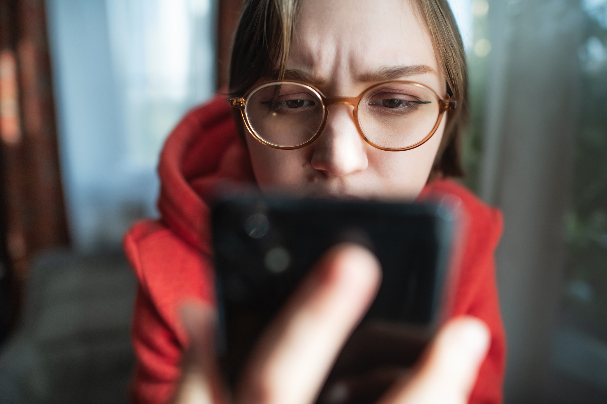 Concerned, sad and worried young woman with smartphone at home reading some bad news or having problems
