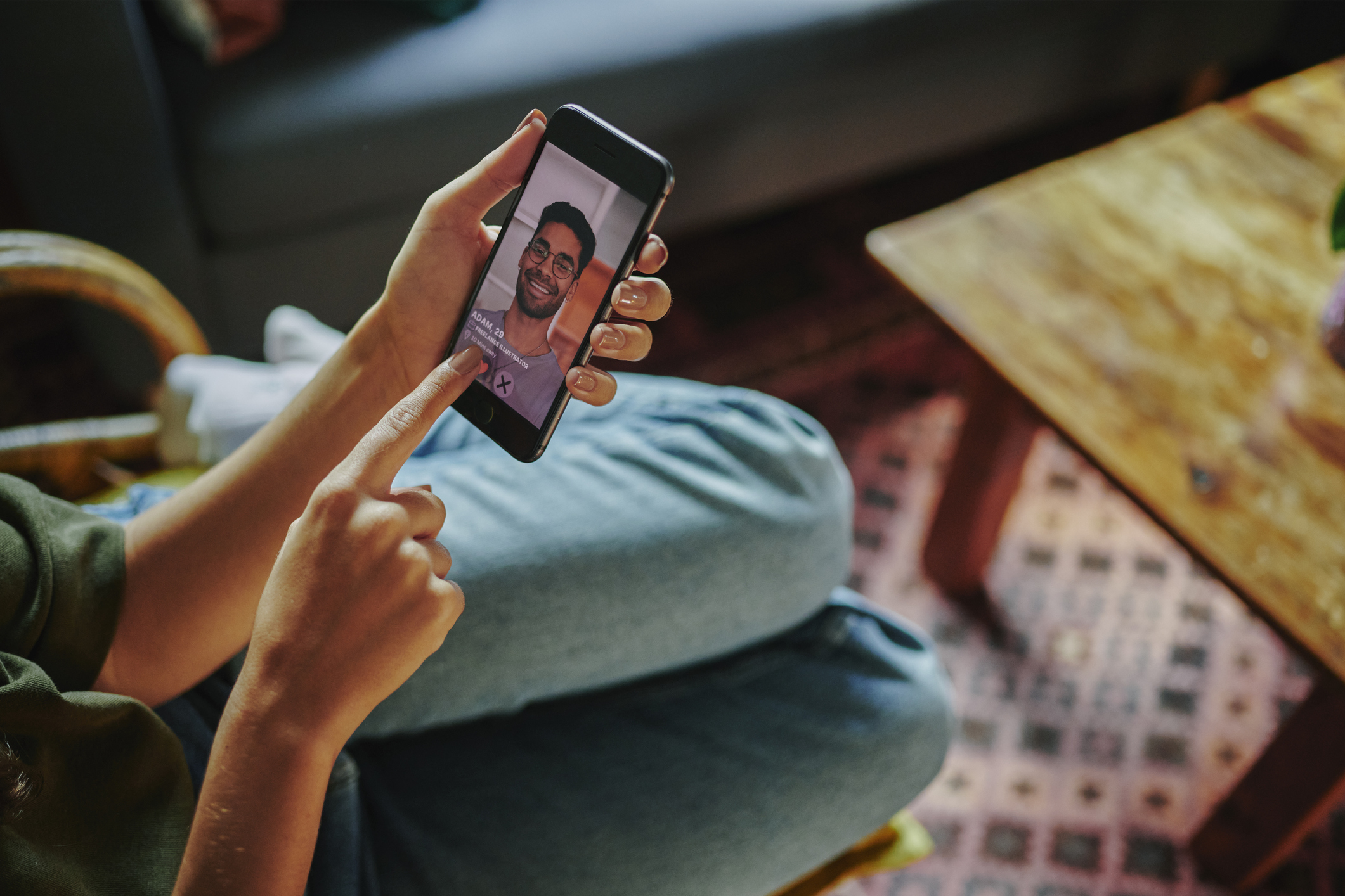 Close-up of a young woman lying on her sofa and liking a man's profile on a dating app on her smart phone