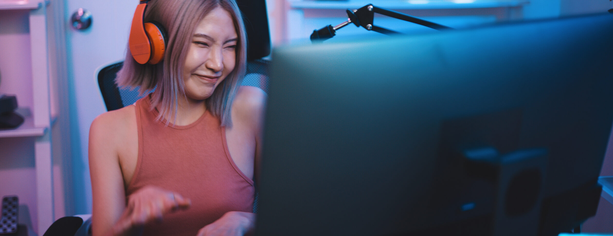 Cheerful Young Asian woman professional gamer wearing headphone to gaming on pc and use microphone to talking with team while has winning in competition, cast gameplay or record a podcast