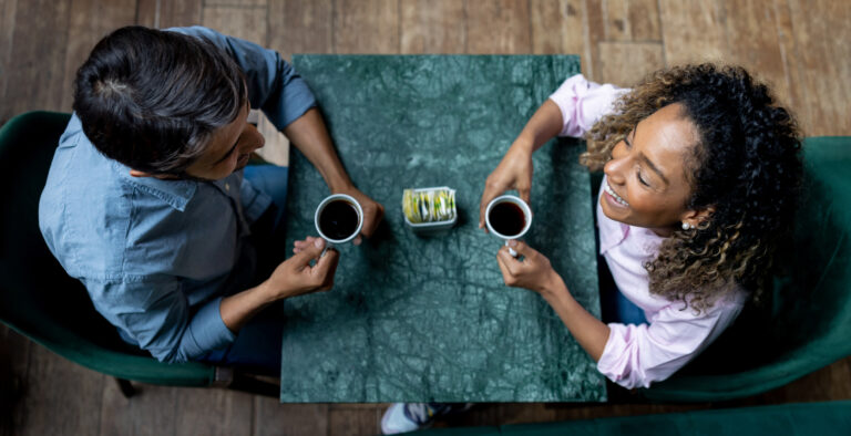 Happy Latin American couple on a date smiling while having a cup of coffee at a cafe